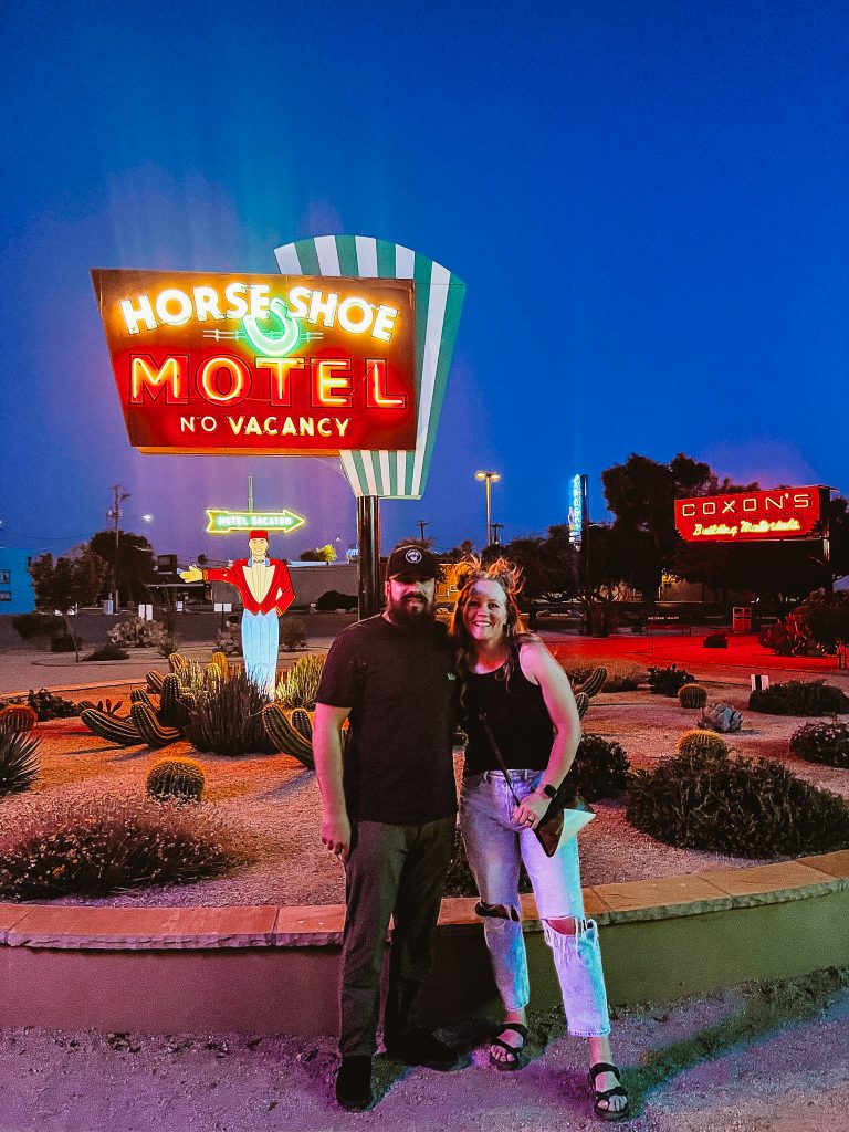 couple standing in front of a vintage neon sign for the horse show motel in casa grande, az